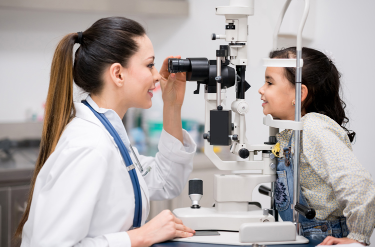 A young female medical optician wearing a white coat is operating a eye health machine and using it on a child in a medical setting