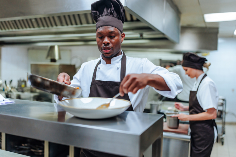 A chef serving up food in a profesional kitchen